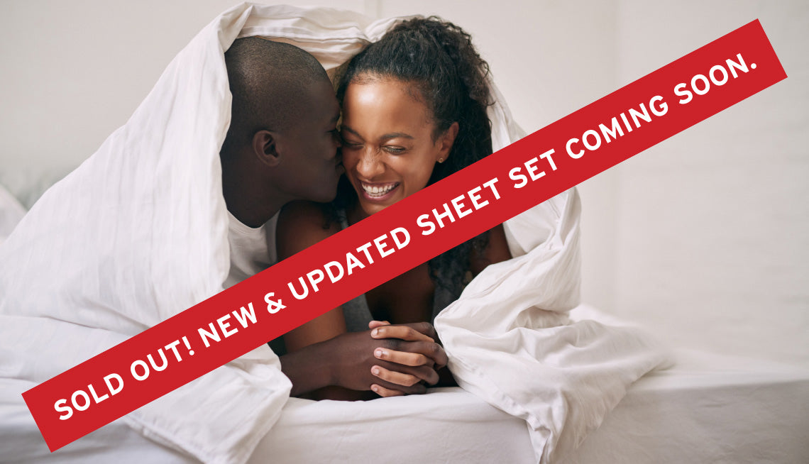 "SOLD OUT! NEW & UPDATED SHEET SET COMING SOON" message over a couple on a bed cuddling under a sateen sheet blanket duvet.