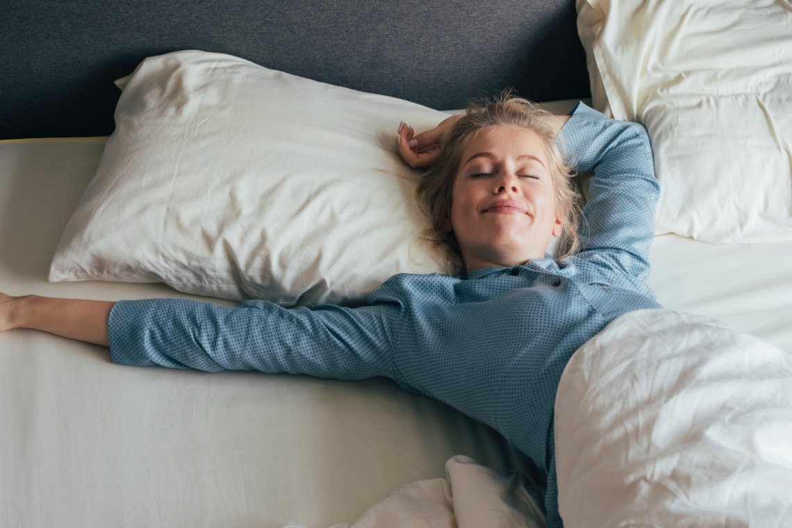 Woman on a bed stretching laying down on ShopTherapedic temp-regulating memory foam pillow. 