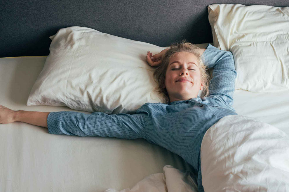 Feeling energized: happy blonde woman in pajamas stretches in bed after waking up in the morning
