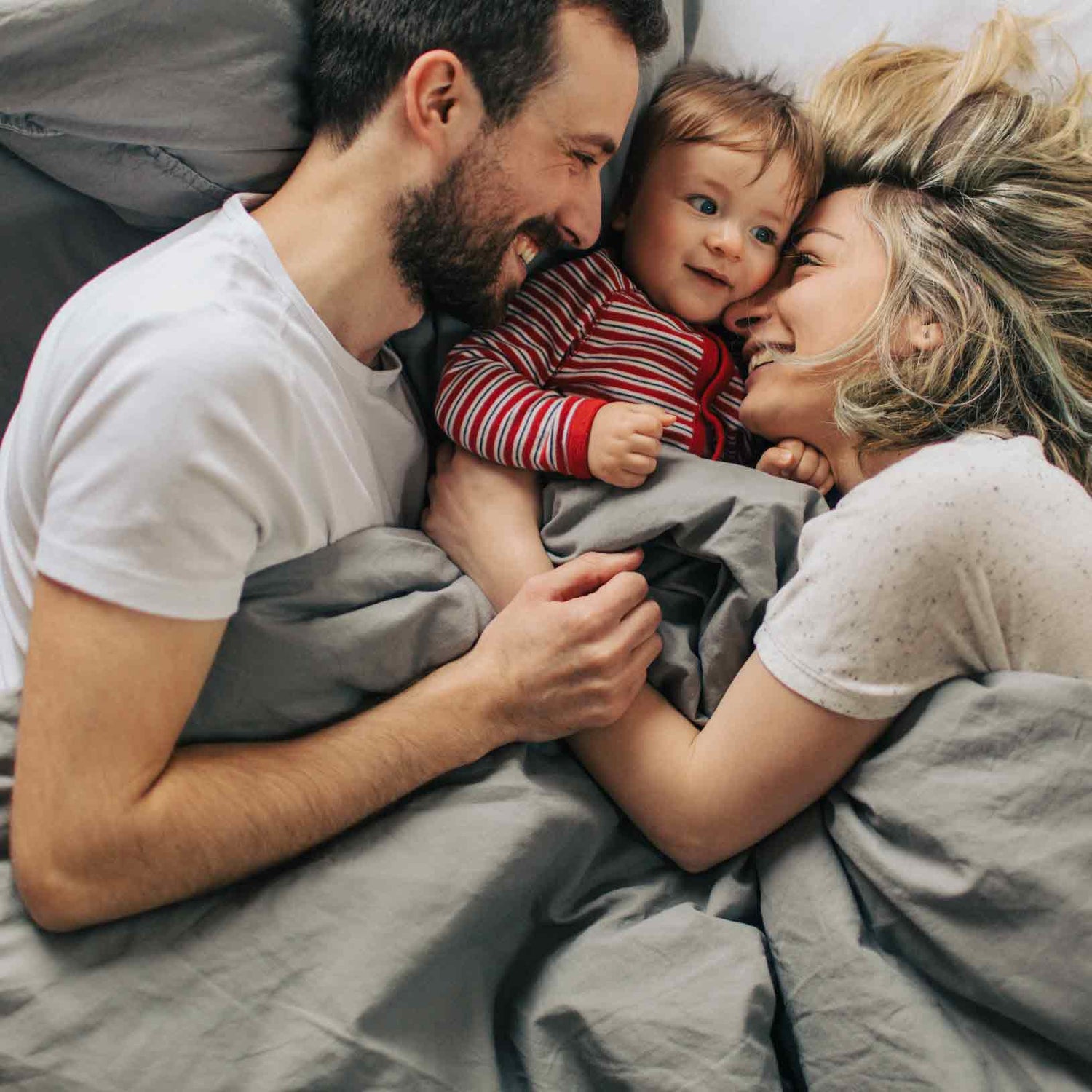 a couple in laying in bed with their toddler between them laughing