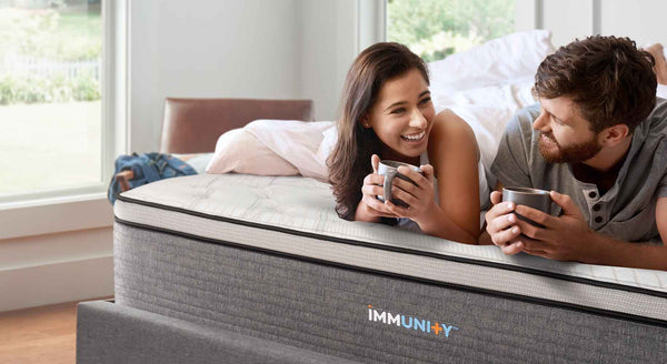 a young couple laying on their new immunity mattress smiling and drinking tea