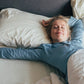 Woman on a bed stretching laying down on ShopTherapedic temp-regulating memory foam pillow. 